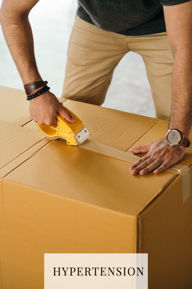 Unrecognizable man sealing box with duck tape while preparing for moving out